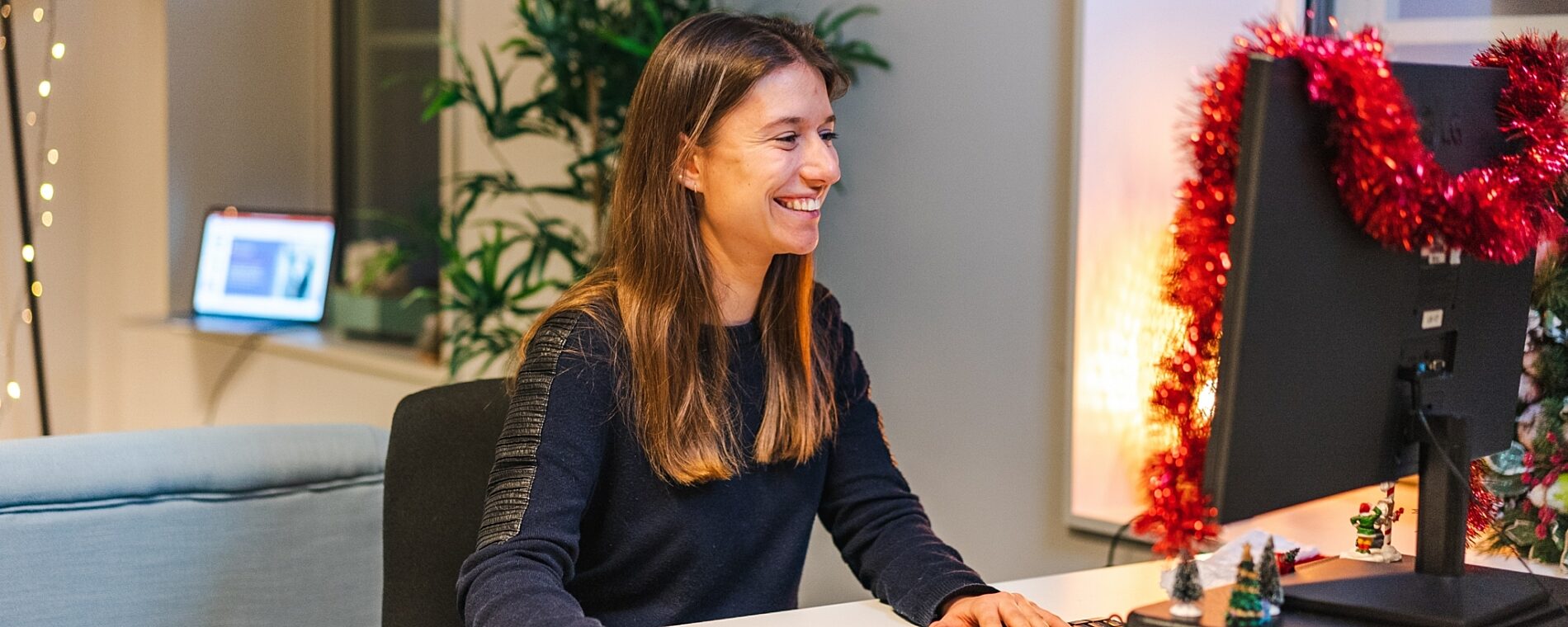 Woman sitting in front of her computer, that's decorated for a winter holiday.