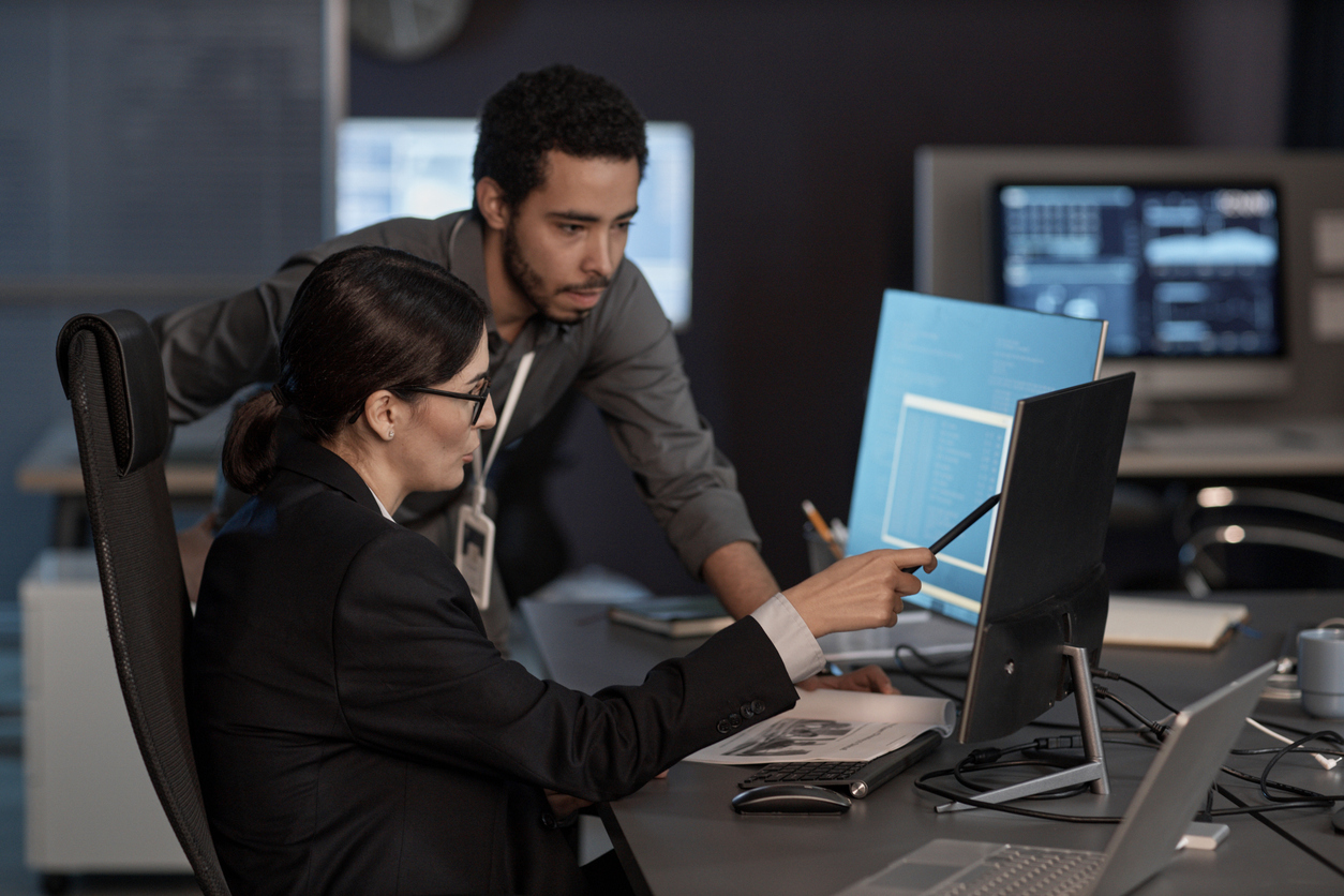 two employees discussing and working on cybersecurity at a computer